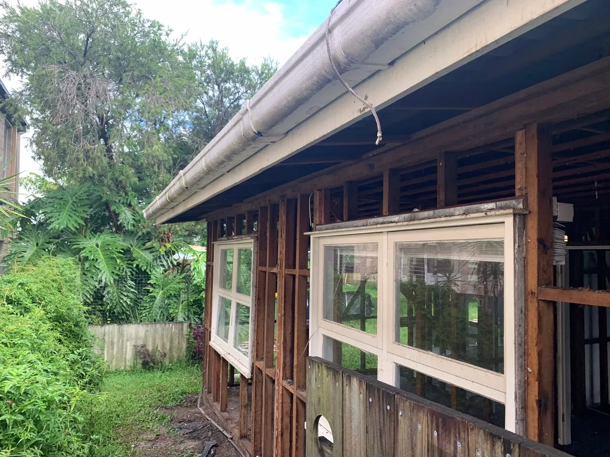 House with exterior cladding removed, exposing timber framing and windows.